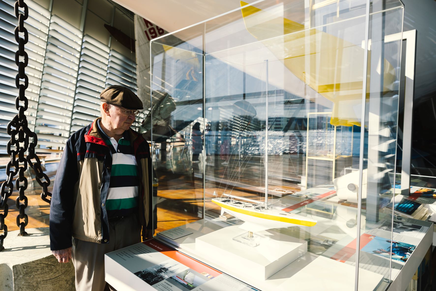 Old gent in hat stairs into glass case holding small boat figurine