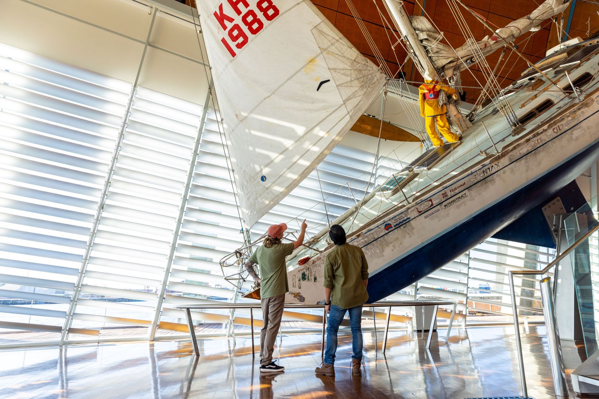 Two men look up at suspended yacht, pointing upward