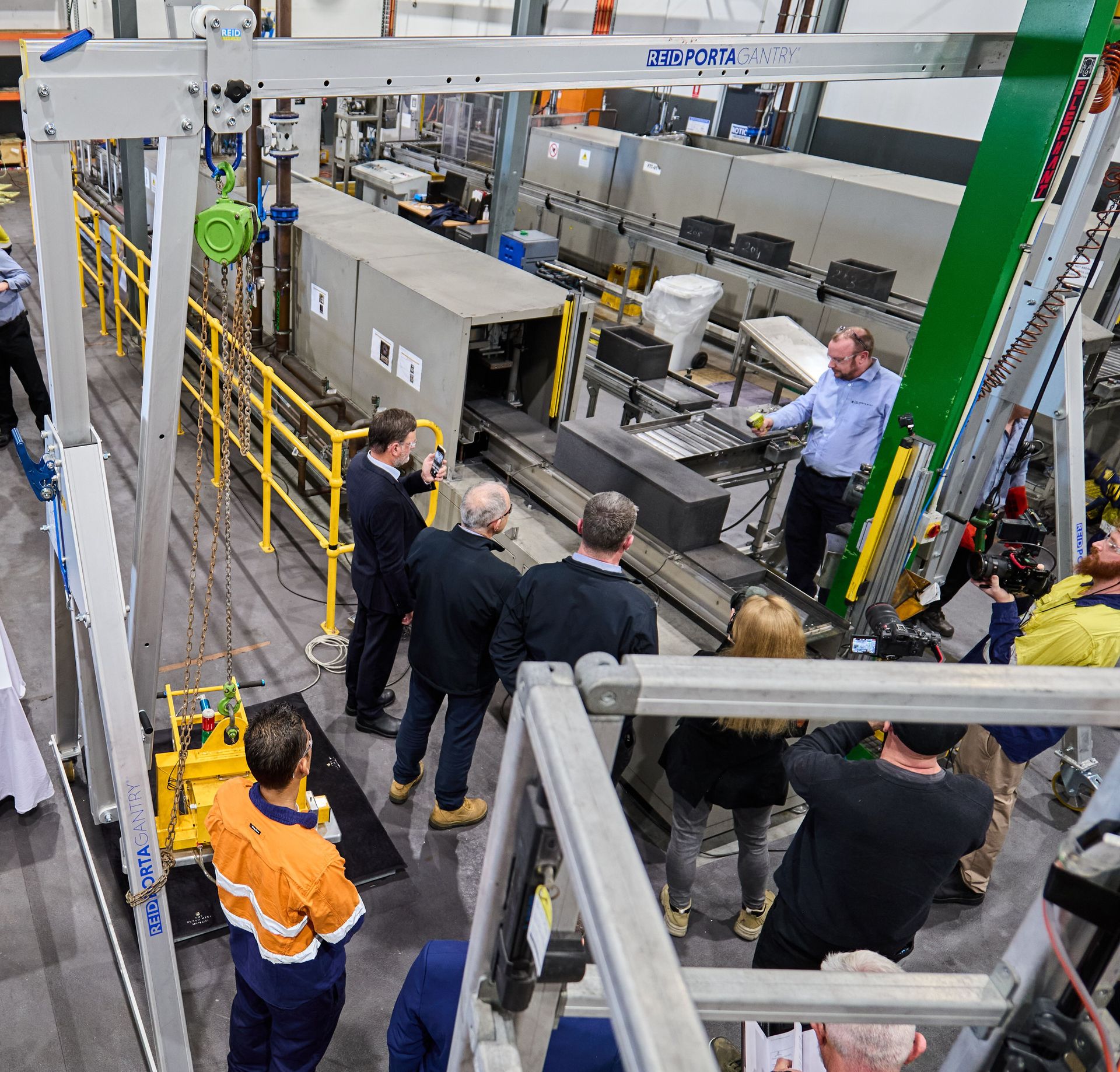 A group of workers in an industrial factory watch as a large mould emerges from a tunnel-like machine called a Flameless Casting Chamber