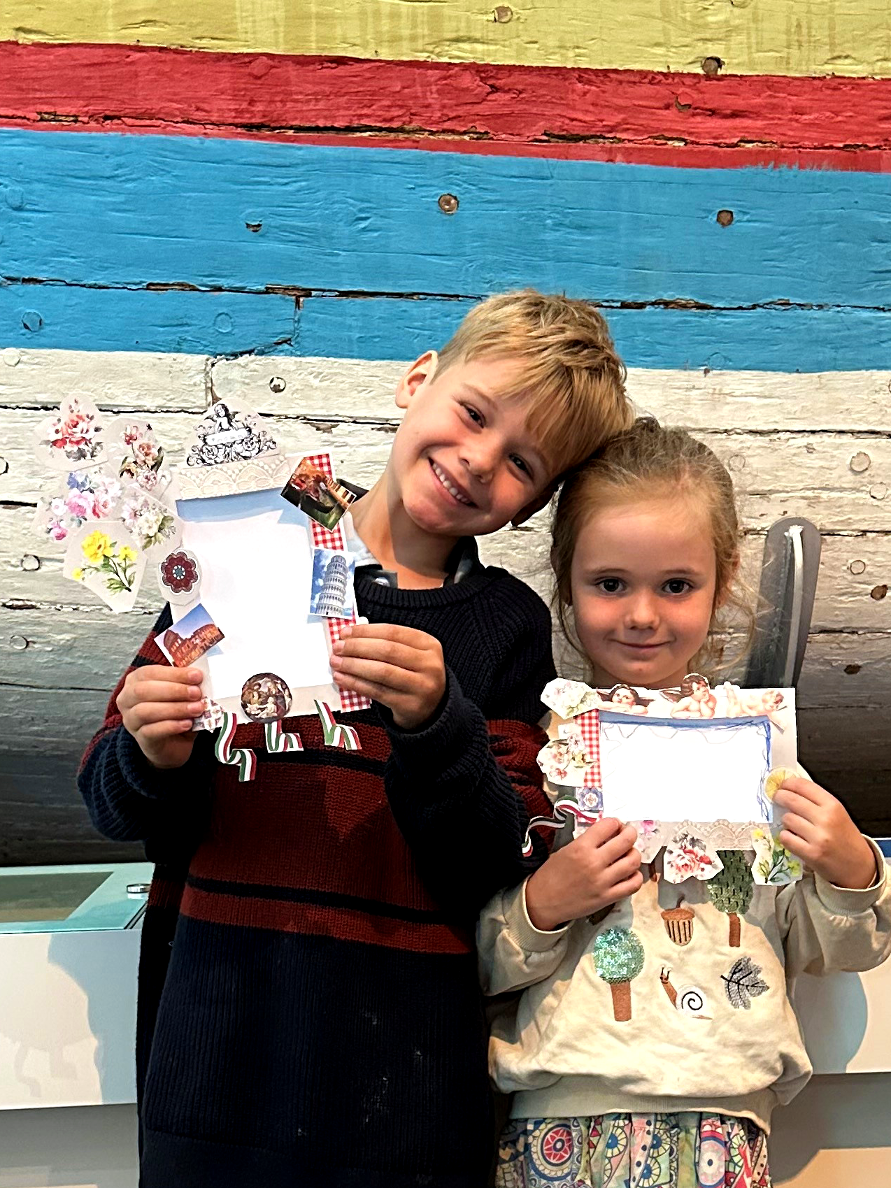 Nonnas Favourites picture frame activity shown held by two young people in front of the Sama Biasa Indonesian fishing boat display at WA Maritime Museum.