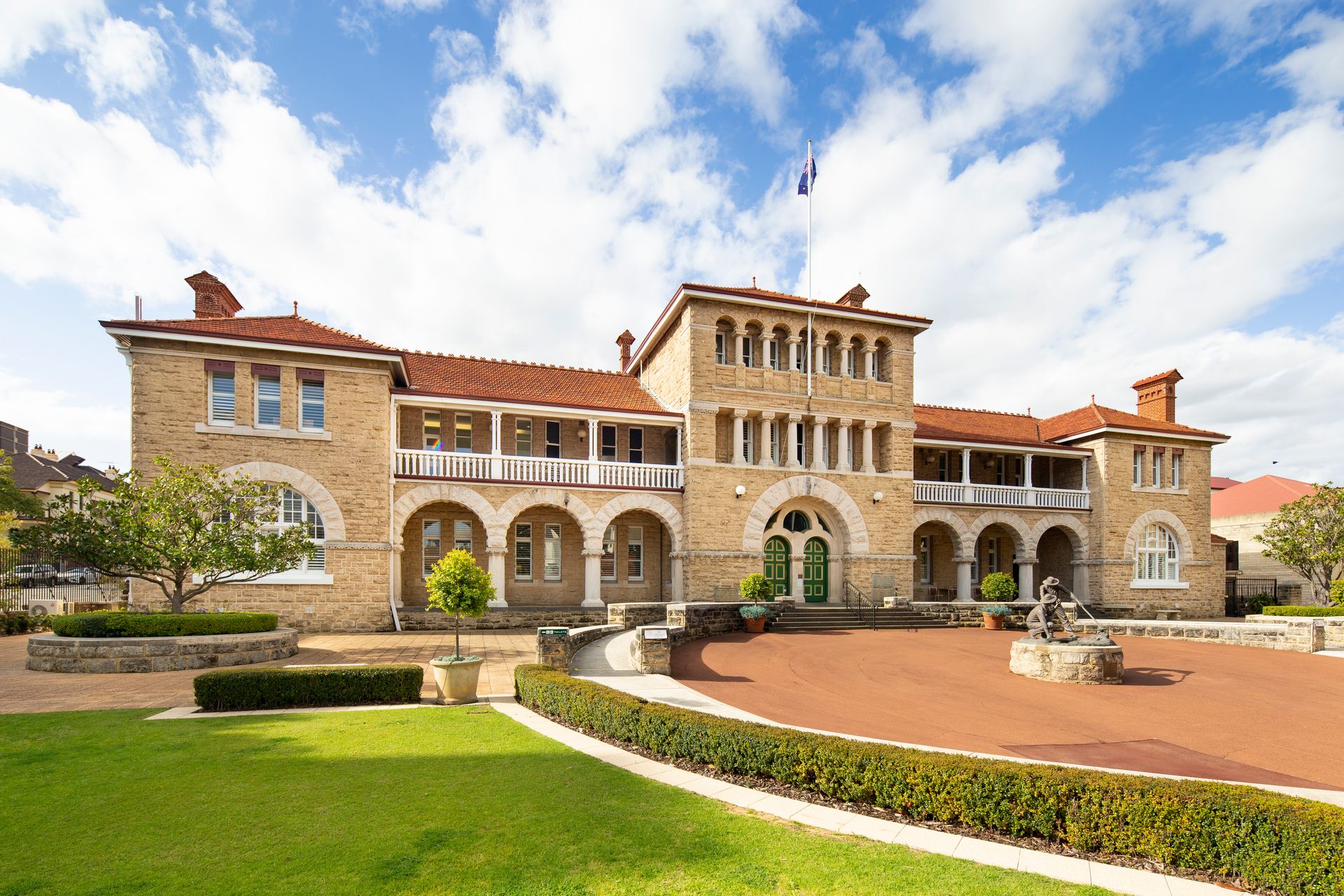 A limestone clad two storey building, with central three storey tower, with an expansive forecourt with lawns and central circular paved area. The building is roofed with orange tiles.