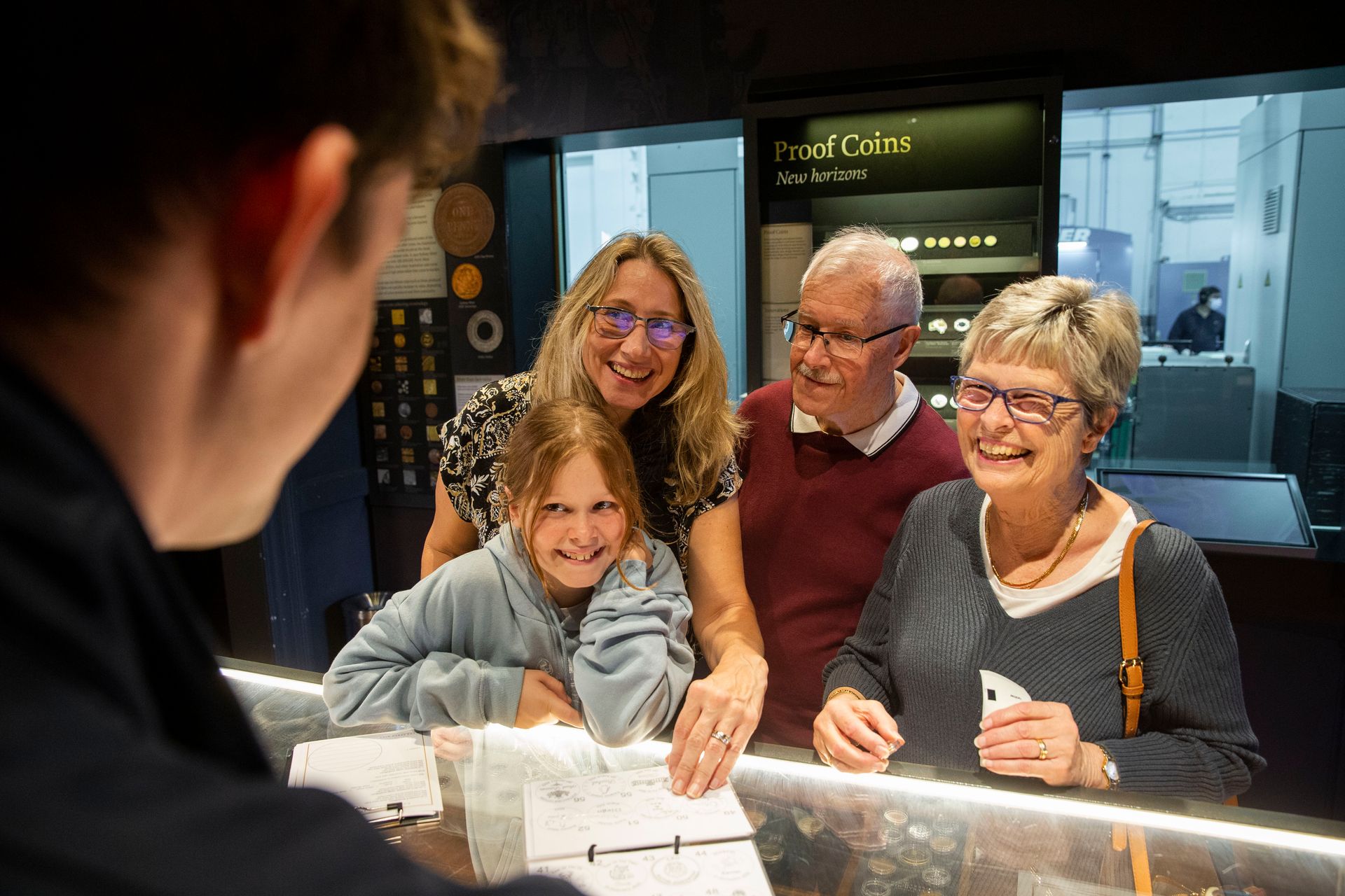 A mother, child and two grandparents stand at a shop counter looking through a booklet of medallion designs and talking to a customer service officer standing behind the counter