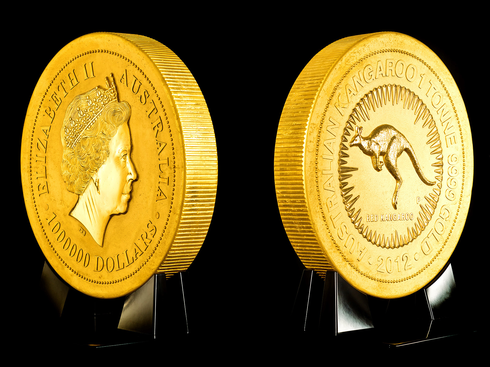 A huge gold coin is standing in black mount. There are two images of the coin - one showing the obverse with the official Royal effigy of Queen Elizabeth II and the reverse with a central design of a jumping kangaroo surrounded by a circle of rays and 'Australian Kangaroo 1 Tonne 9999 Gold 2012'