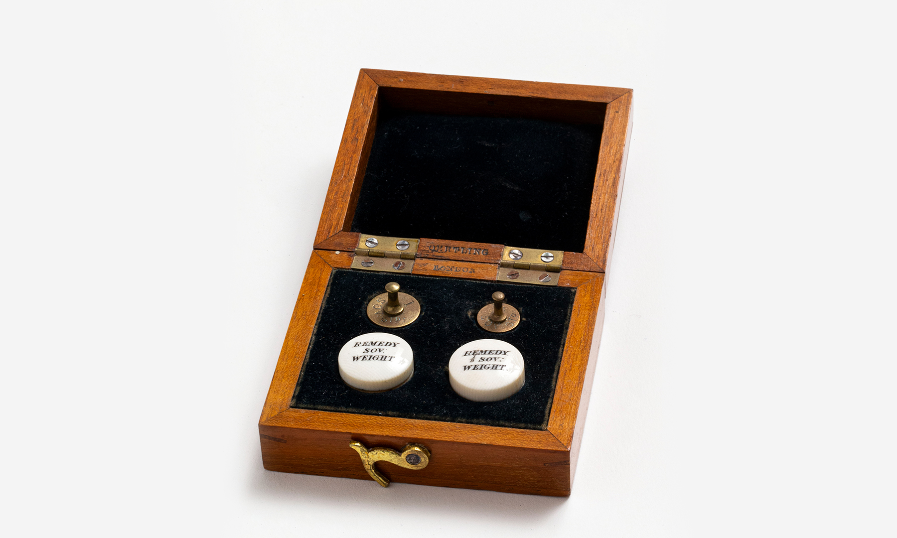 Wooden velvet lined box with hinged lid containing two metal weights, one for a sovereign and one for a half sovereign with two small white cylindrical containers marked 'REMEDY SOV. WEIGHT' and 'REMEDY 1/2 SOV WEIGHT'