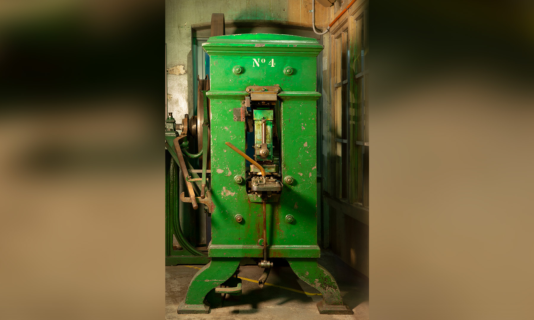 A tall narrow old piece of industrial machinery with large flywheel, painted green with 'No. 4 at the top'
