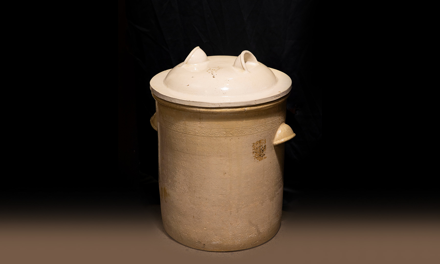 A large ceramic pot with curved ceramic lug handles and ceramic lid also with two ceramic lug handles