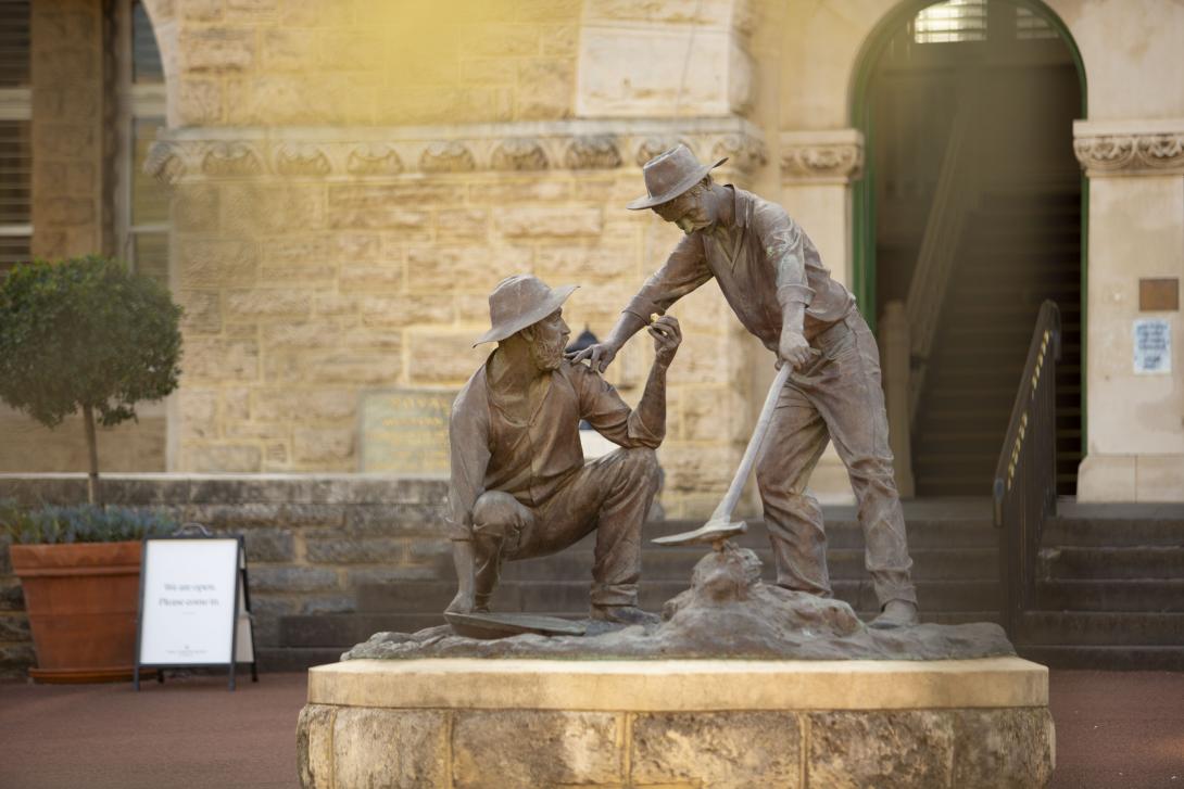 Bronze statue called 'The Strike' of two prospectors by sculptor Greg James. One figure is crouching and holding up a small gold nugget to the standing figure, who looks upon it with exciutment.