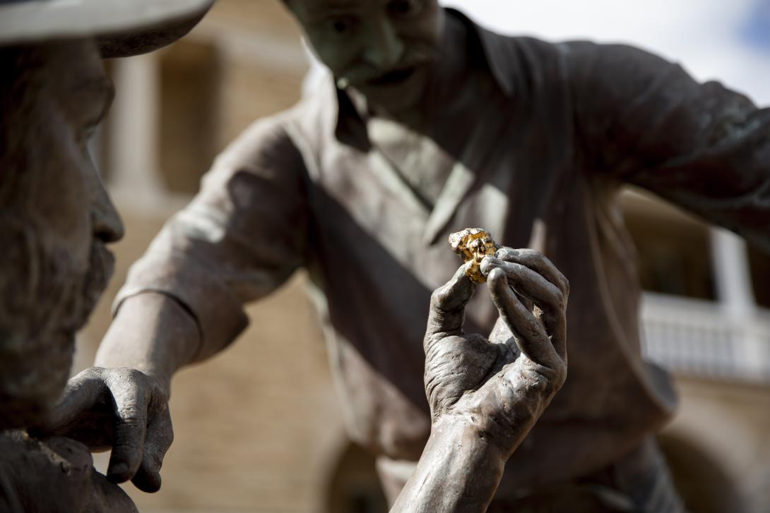 Detail image of 'The Strike' bronze statue in the forecourt of The Perth Mint - a man's hand holds up a gold nugget to show it to a mate who is touching his shoulder. Both men have an expression of surprise.