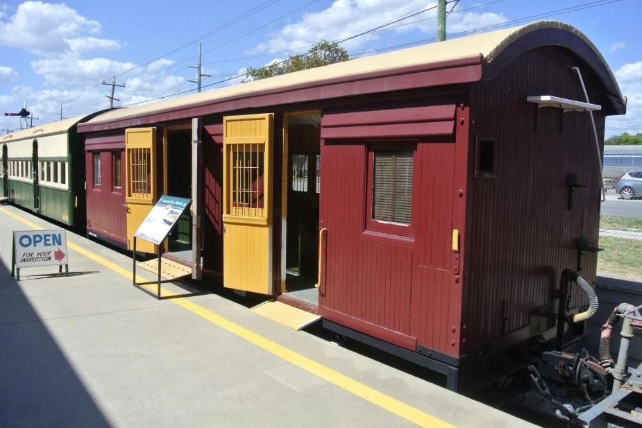 Timber rail carriage on display in an outdoor museum, carriage is painted burgandy  with two yellow doors and white roof. All windows have metal security bars