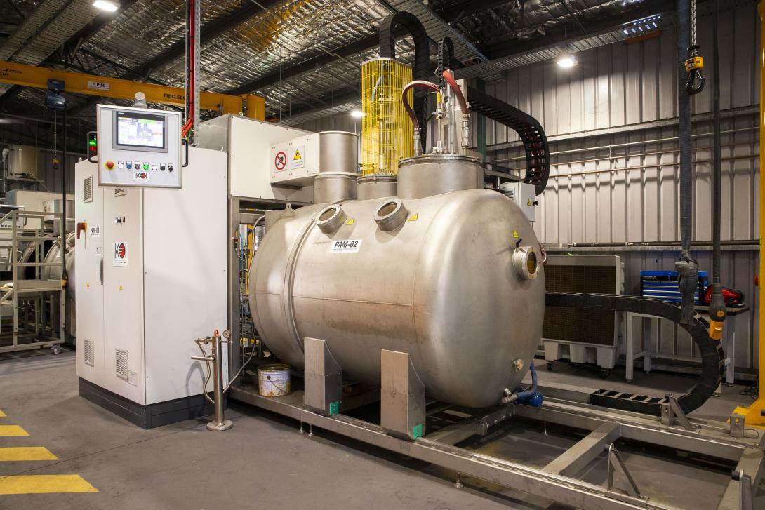 View inside an industrial factory with a large piece of machinery that has a cylindrical chamber on tracks at the front