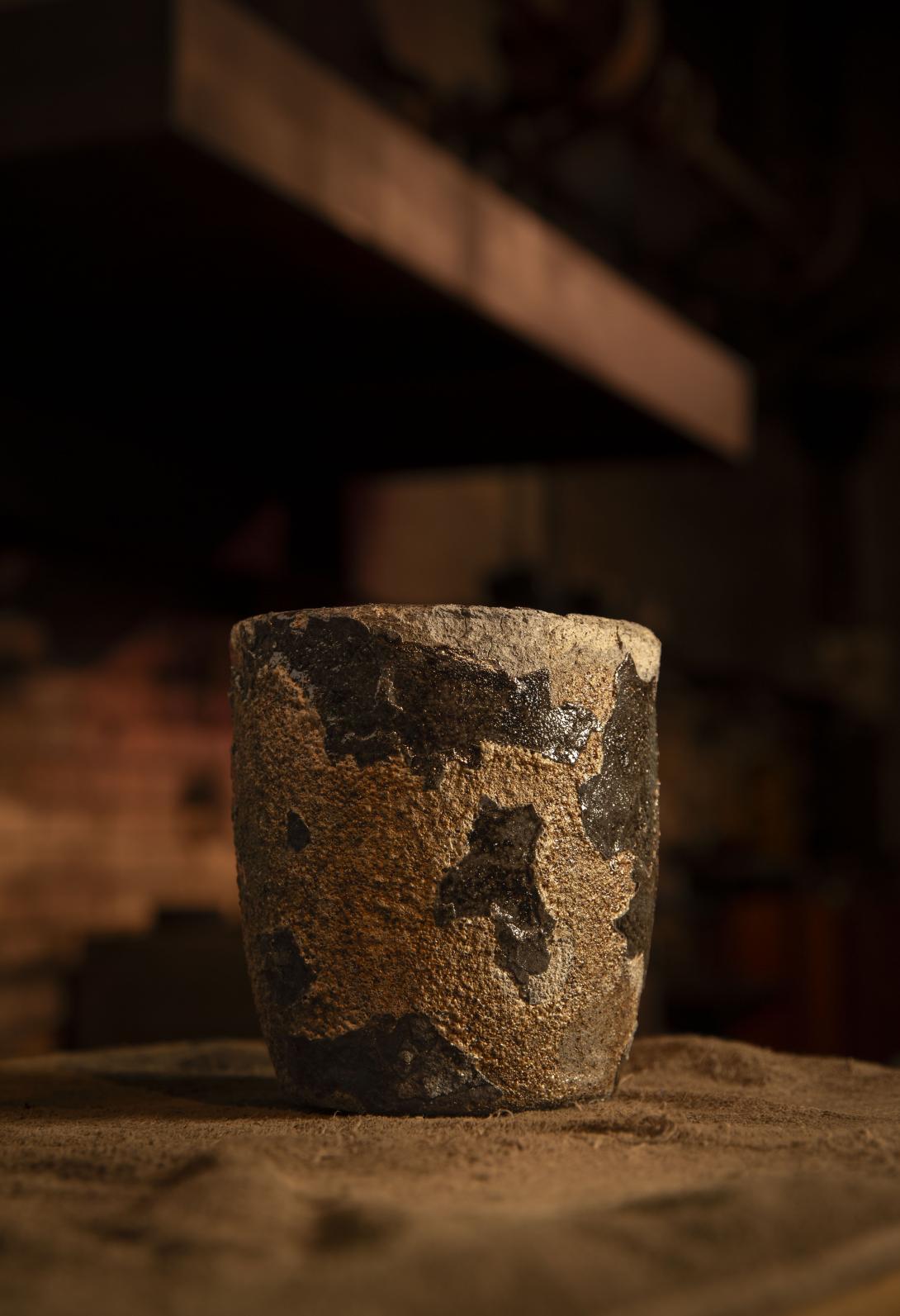 A used clay and graphite crucible rests on top of a furnace