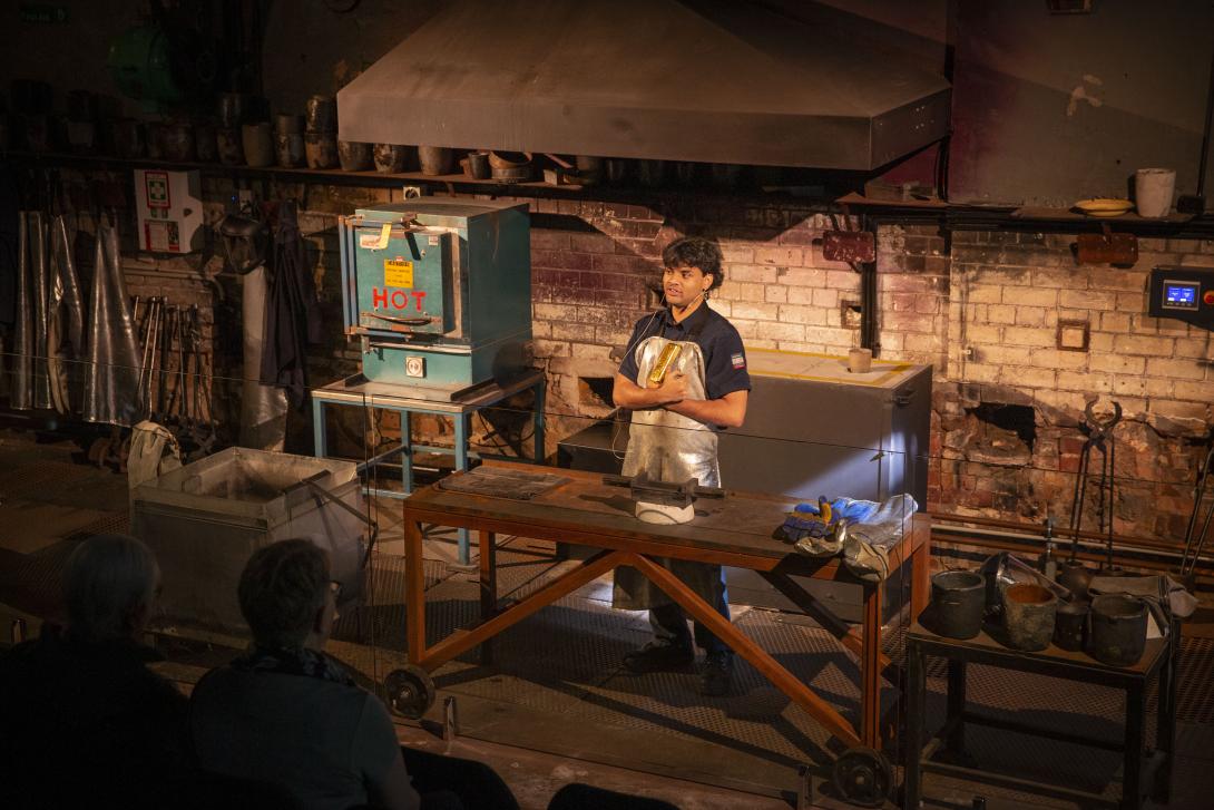 A male gold pourer stands in an industrial melting house holding a cast gold bar
