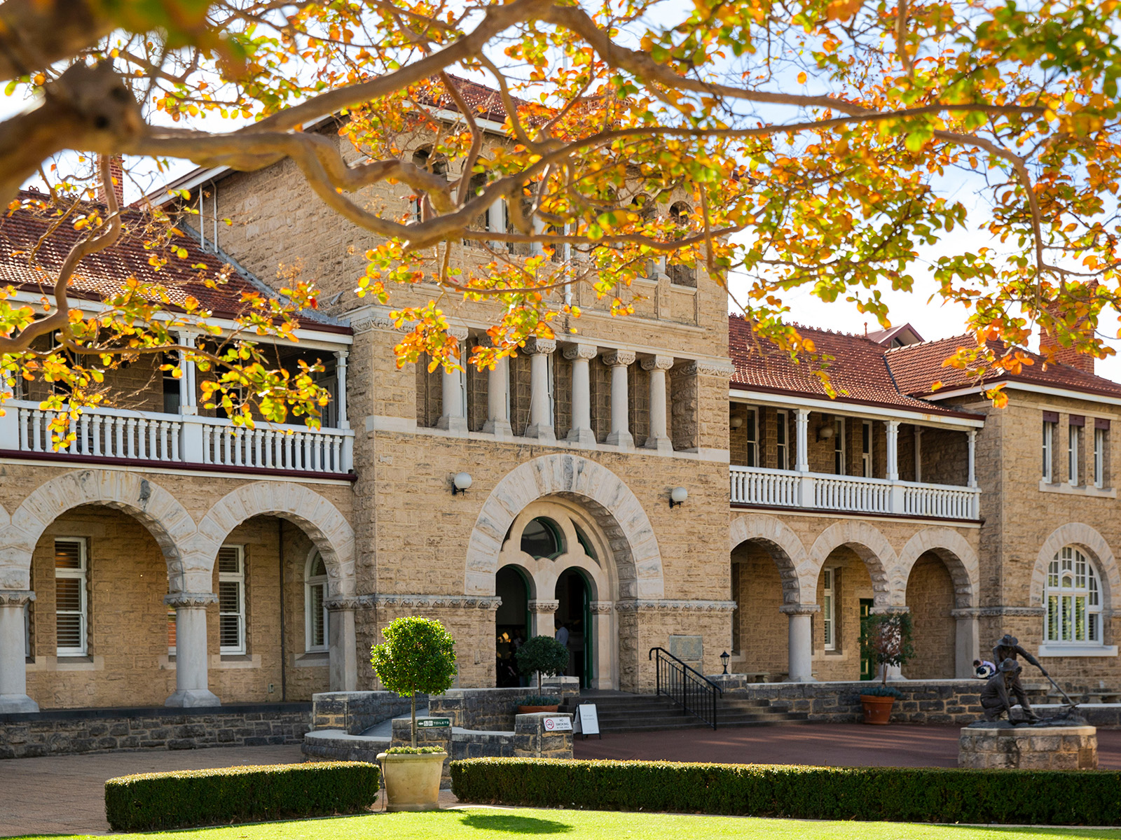 Two storey building with three storey central tower, limestone facade, orange tiled roof, tree with autumn leaves in foreground
