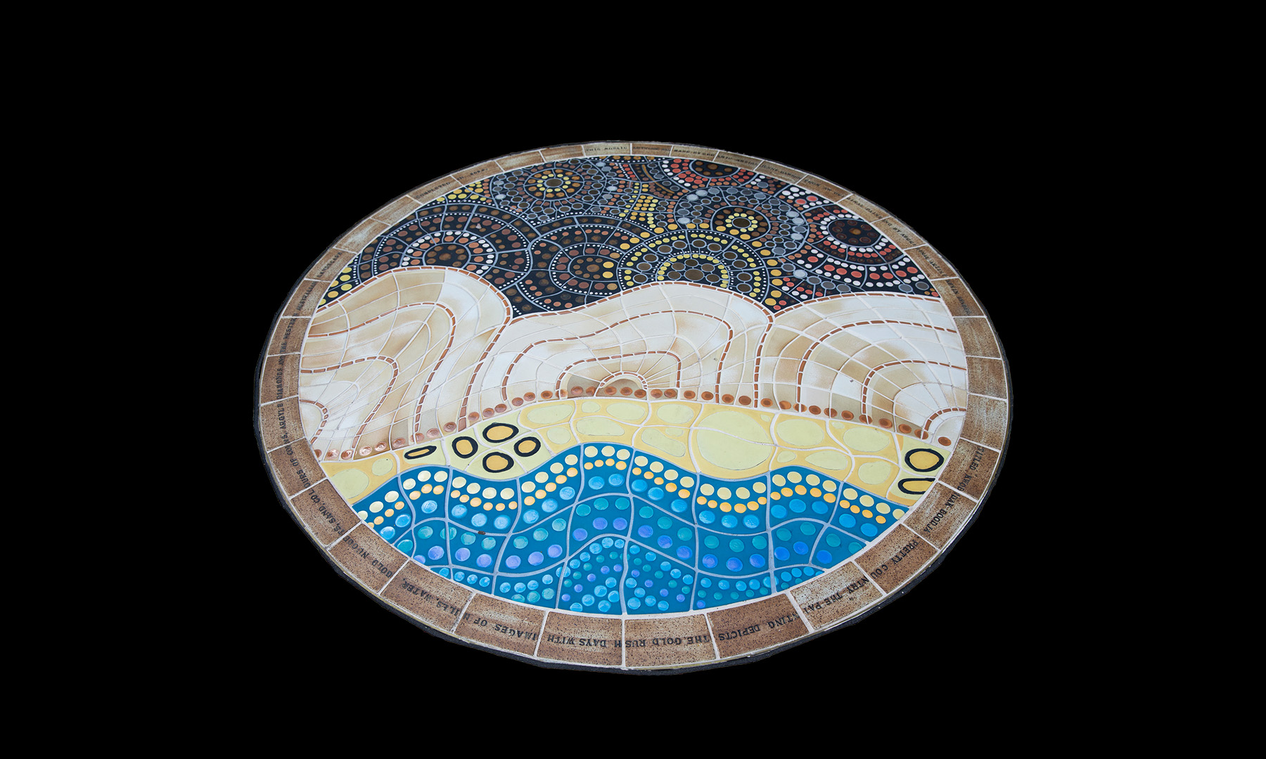 A circular mosaic artwork inlaid on the ground made of small tiles - the lower section has a design of blue and yellow tiles that depicts the gold rush days with images of hills, water, sand, and golden nuggets. The upper part of the mosaic includes shades of gold and silver - depicting coins.