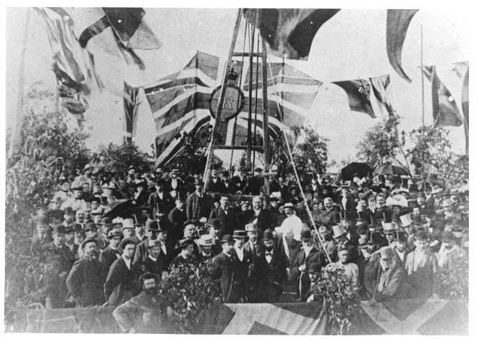 Black and white image from 1896 showing a group of people formally dressed surrounded by flag bunting, including a large central Union Jack with ER in the centre.