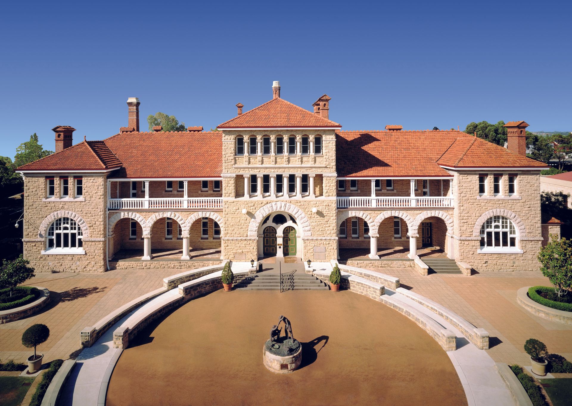 View of large two storey building with three storey central tower and large forecourt with central statue