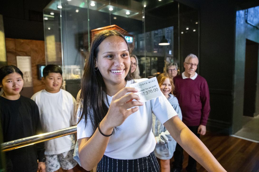 A girl holds up a printout of her weight calculated using the live gold price, which is $4,787,370.00, while other visitors look on.