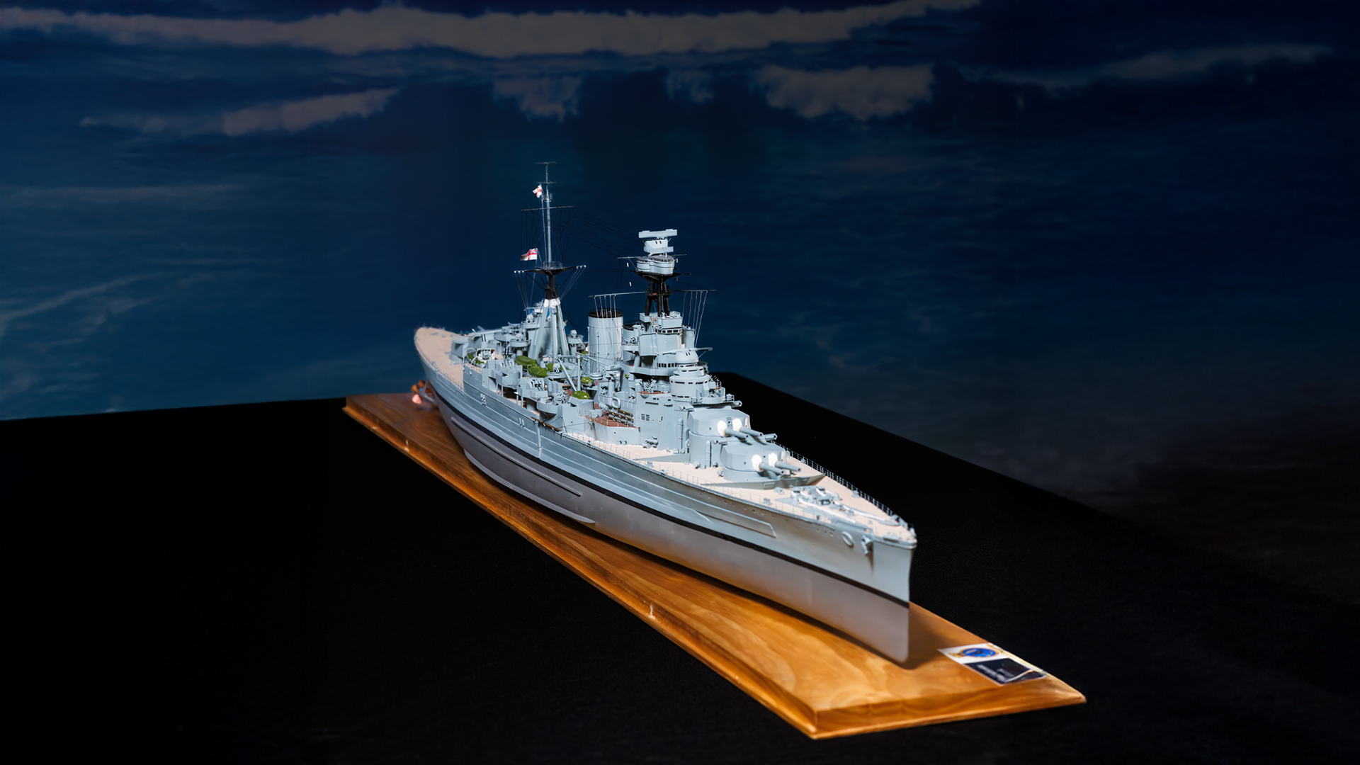 Miniature model naval ship displayed on a wooden base with a dark background.