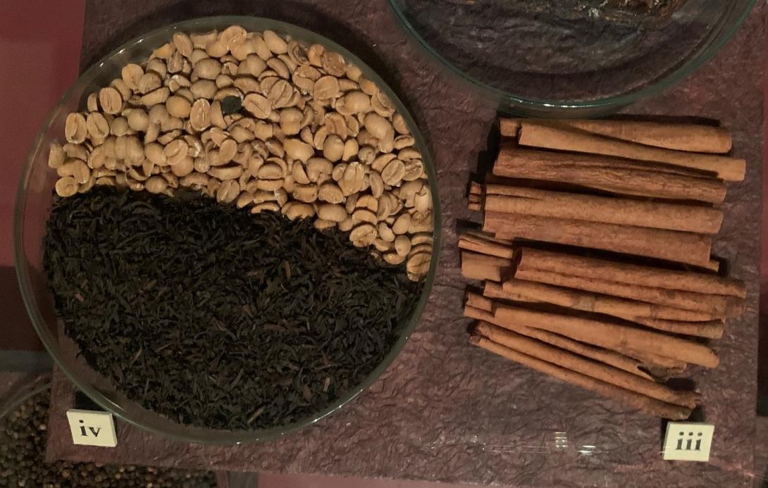 A display of spices in a cabinet, including cinnamon quills, tea and coffee.