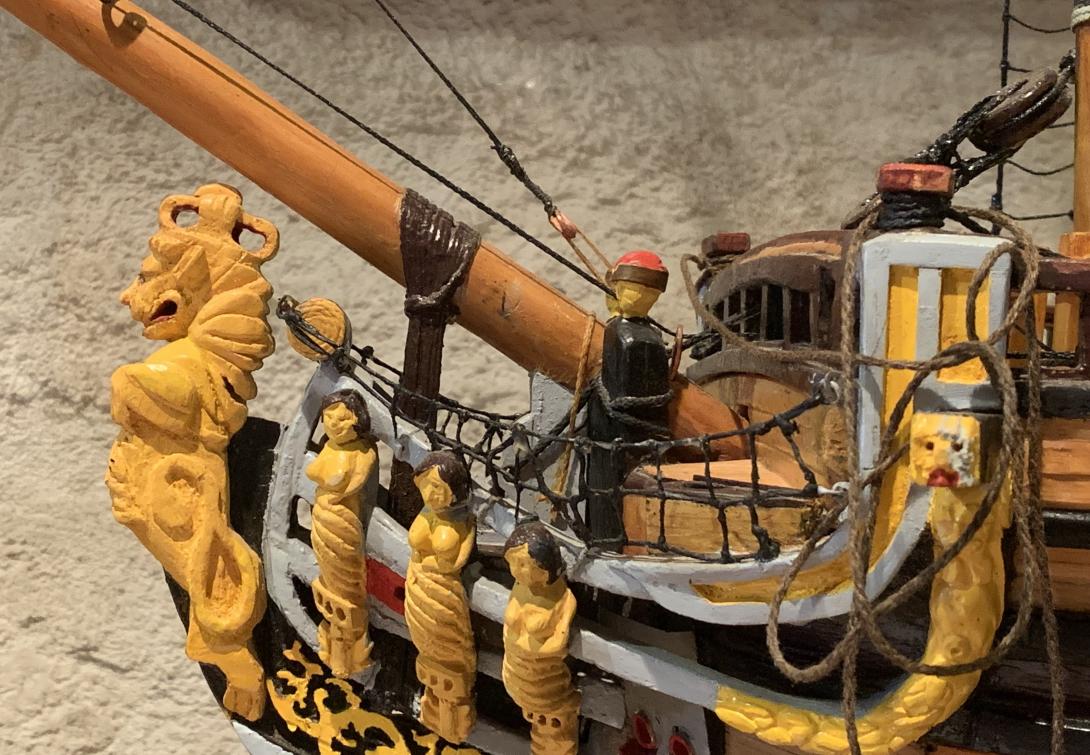 Yellow carved figures of topless women and a lion figurehead on a model of the ship 'Roebuck'.