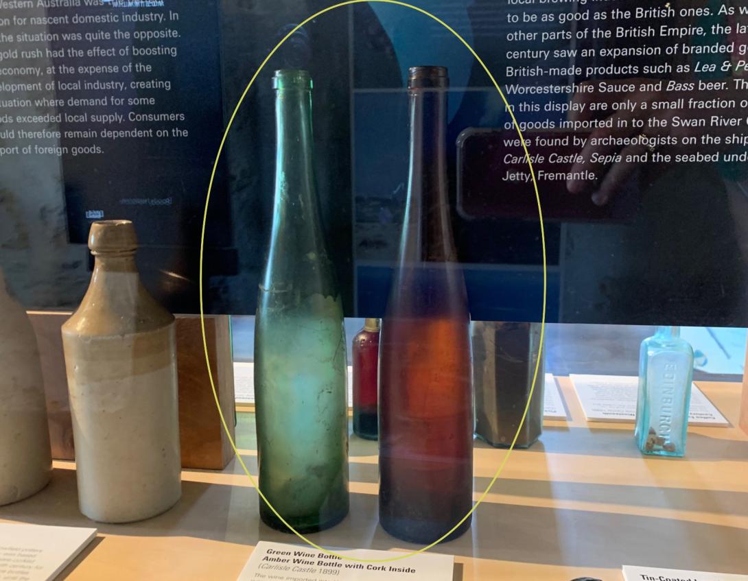 A green wine bottle and an amber bottle with a cork inside.