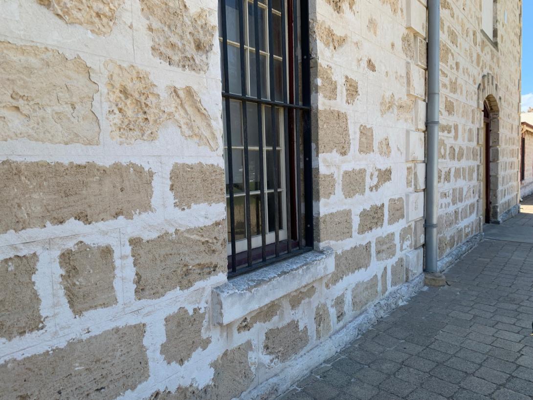 A sash-window in a limestone brick building. It is fitted with heavy duty, old fashioned iron security bars.