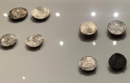 Eight silver coins from shipwrecks, some shiny, others tarnished and blackened with age.age of