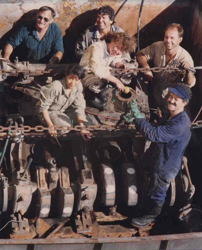 Photo taking from view looking down at six smiling people who are standing around large piece of machinery.