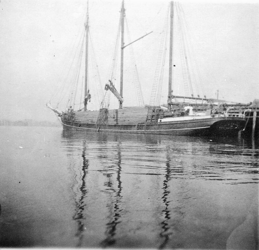 A sailing ship with three masts heavily loaded with planks of timber.