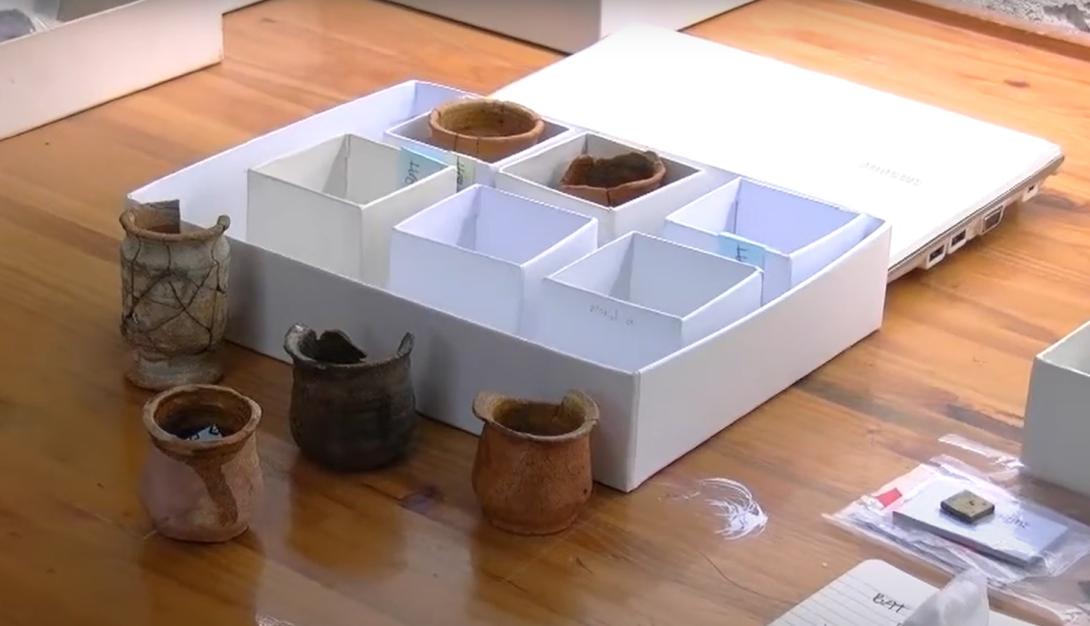 A white cardboard box holds a number of small jars, most are cracked near the top lip.
