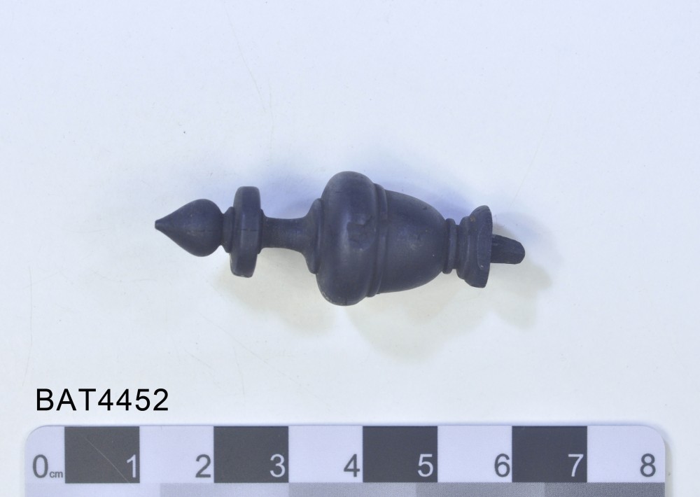A black wooden chess piece in the Museum display cabinet. There is a small chip in the side of the piece.