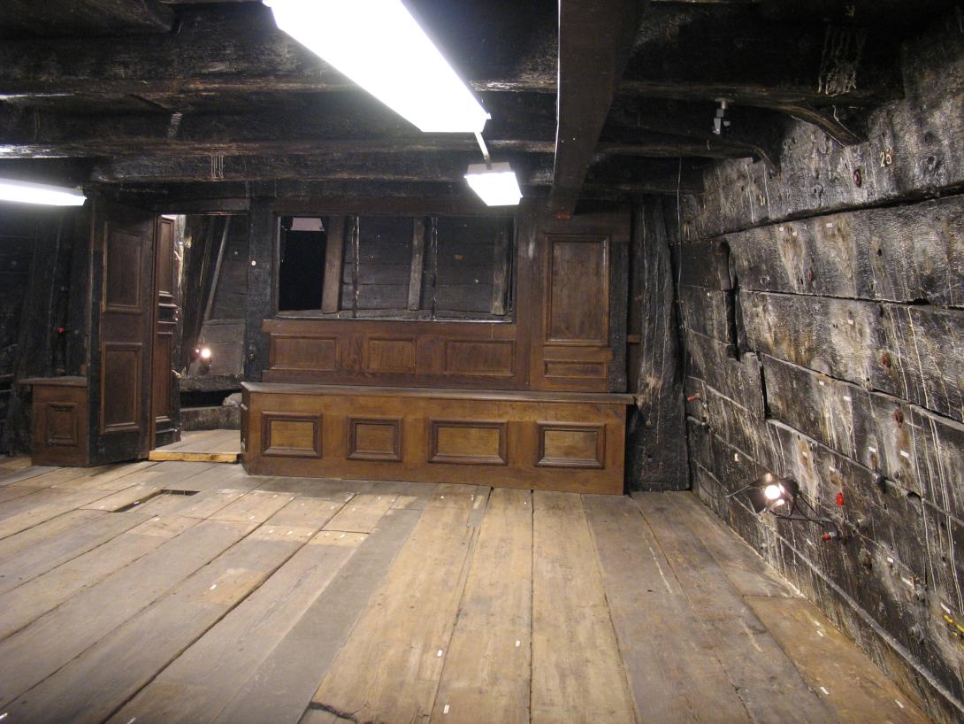 A large cabin, heavy wear is visible on the shipwreck's timbers. There is a fine cabinet against the wall.