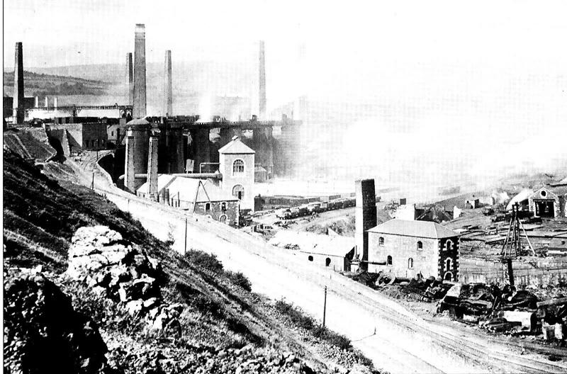 Smoke from many large chimneys obscures some of the brick buildings in this large factory complex.