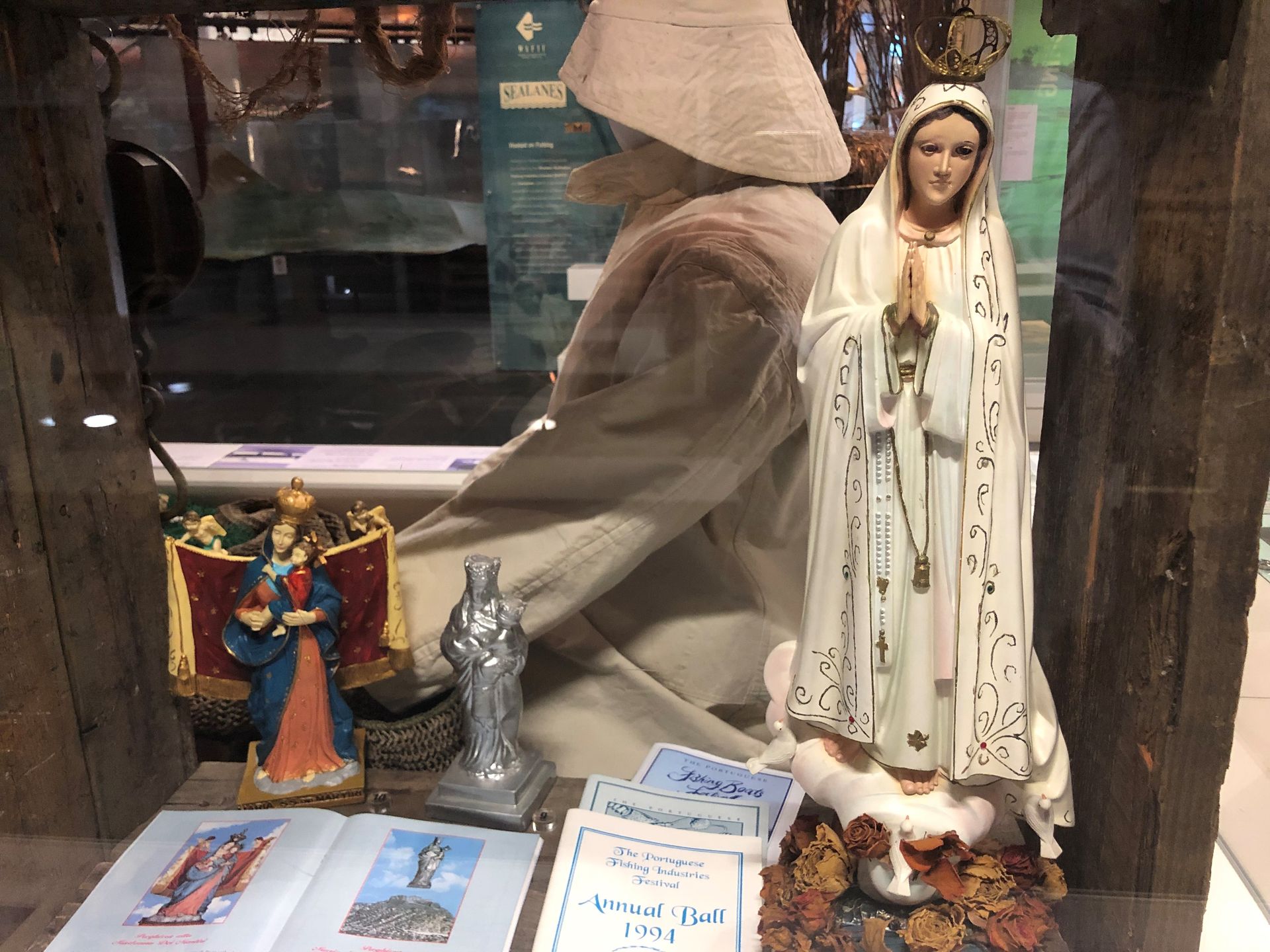 Religious statues in a display case, a mannequin in white clothing can be seen on the opposite side of the case.