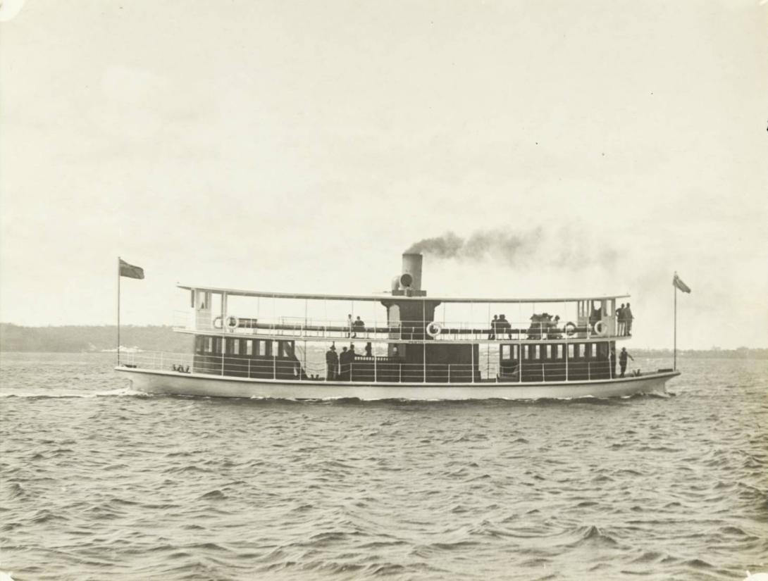 A view of the side of the ferry. Passengers can be seen sitting leisurely on the long bench extending across the length of the top deck.