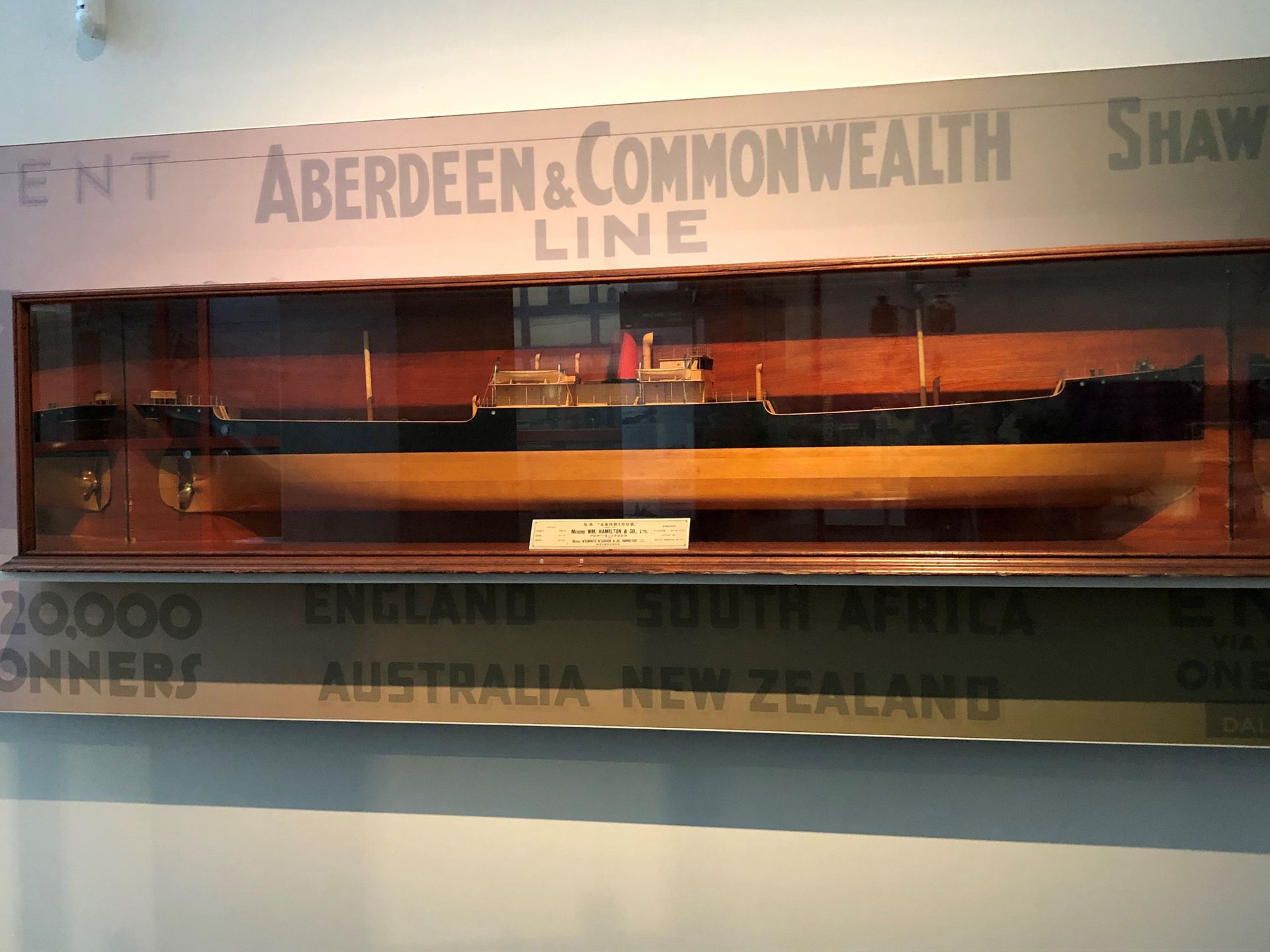 A large model of a black and brown wooden ship in a glass display case, mounted on the wall. Large tet above reads "Aberdeen and Commonwealth Line."