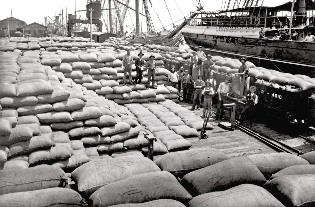 group of men on the wharf, surrounded by stacks of sacks.