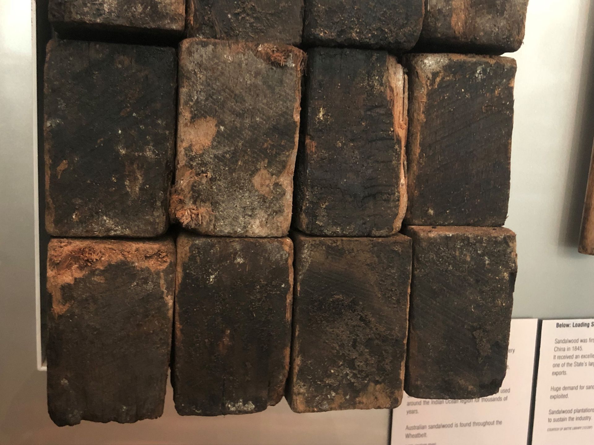 A stack of darkened brick-shaped blocks of wood are mounted on the Museum's wall.