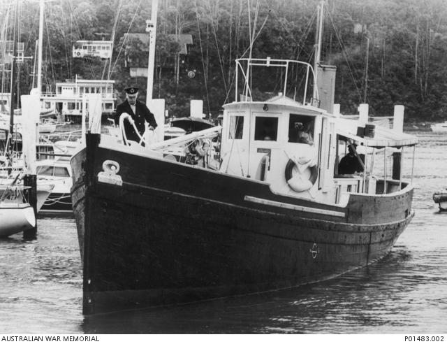 A nicely painted wooden boat in harbour, attended to by a sailor in a dark uniform and hat.