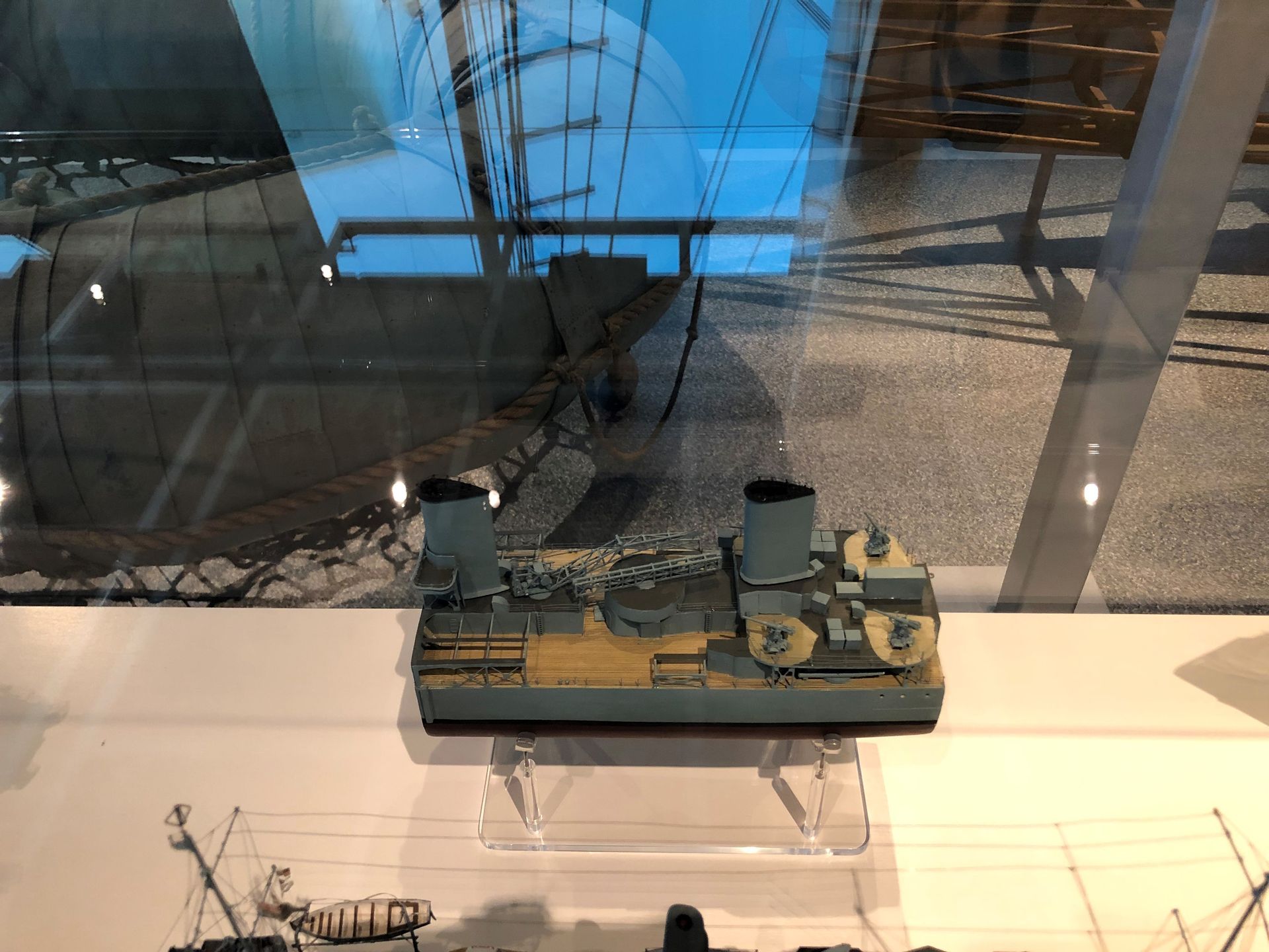In a display case is a small section of a ship model. The model ship is painted grey, the section has two funnels and a wooden deck.