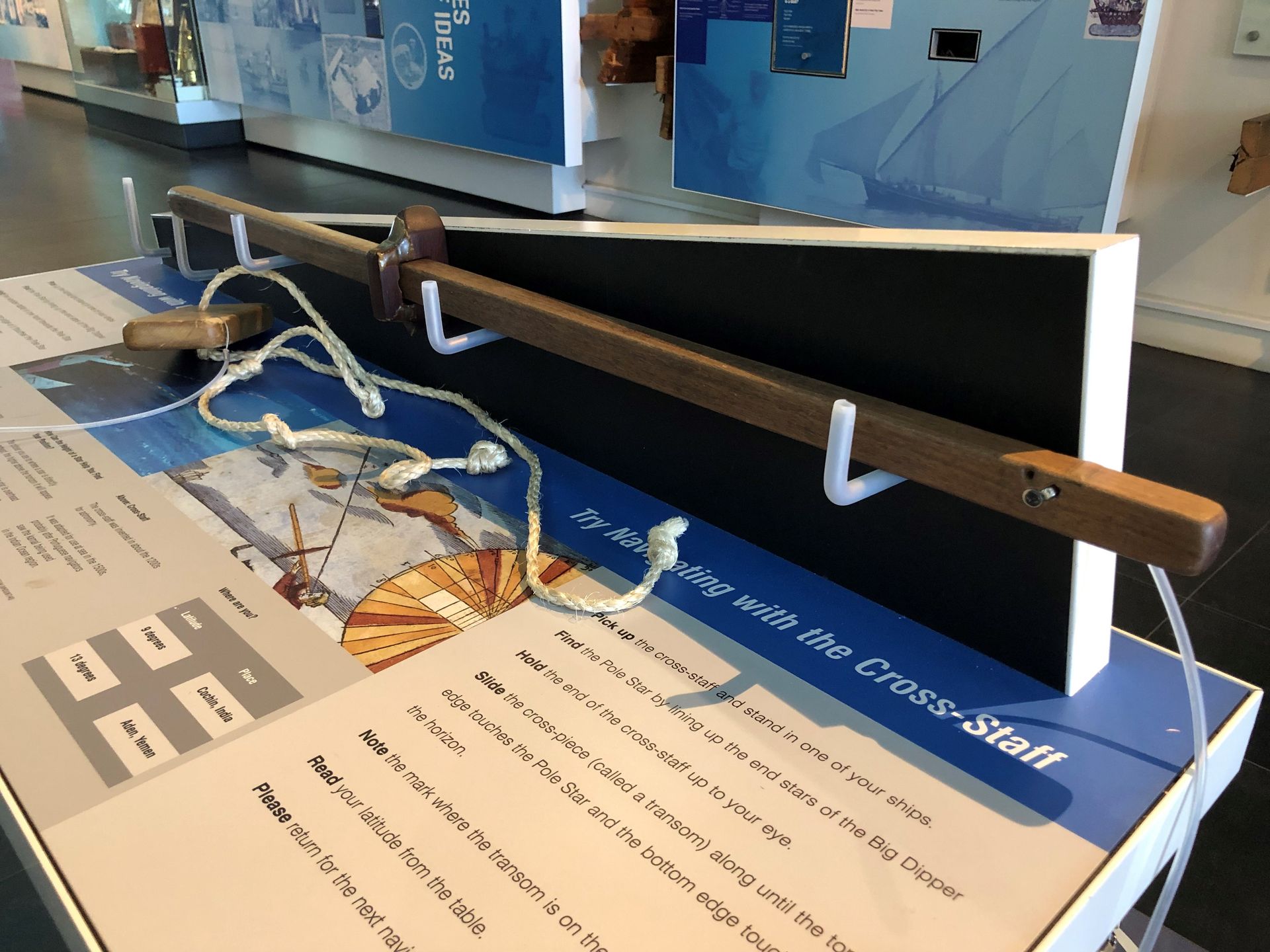 A long thin wooden rod attached to the display with a rope. There is a piece of wood on the rod you can move back and forth. The display reads 'try navigating with the cross-staff.'